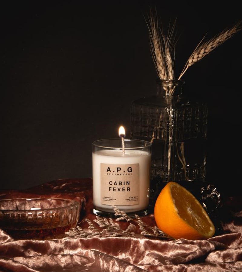 Photo of a white candle in a glass jar on a velvet fabric next to a sliced orange 