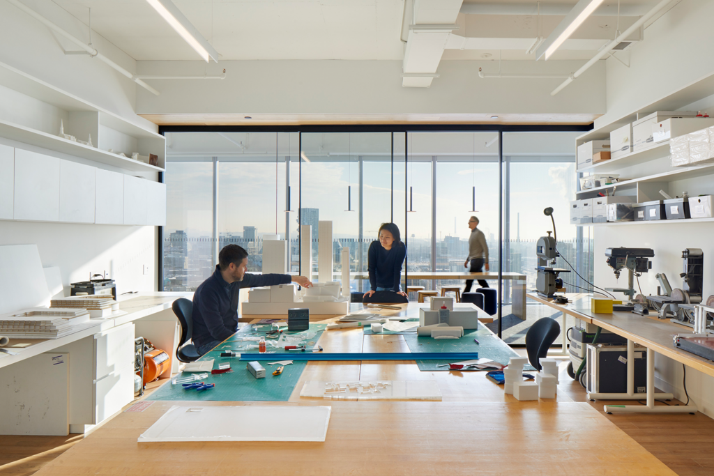 A photo of people working at a communal table in the center of an office